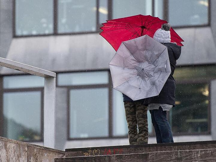 Zwei Passanten hantieren mit ihren Regenschirmen. Foto: Marijan Murat/dpa/Archivbild