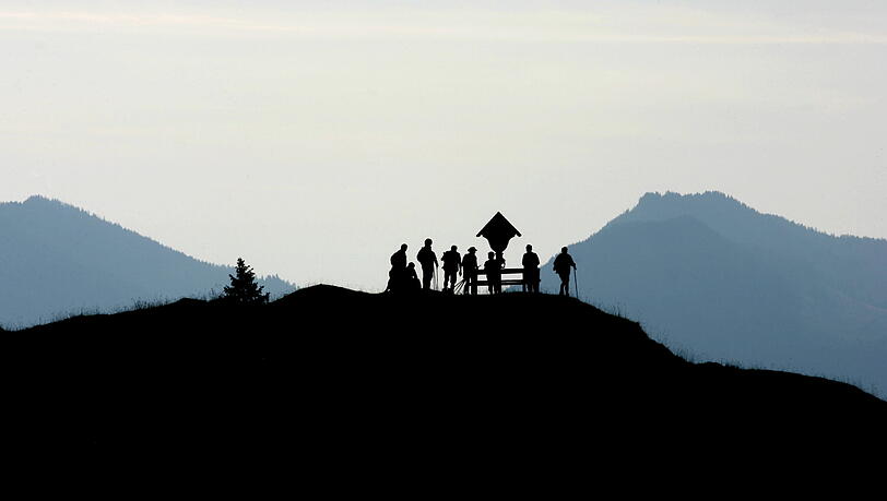 Bergwanderer stehen am frühen Morgen an einem Wetterkreuz .