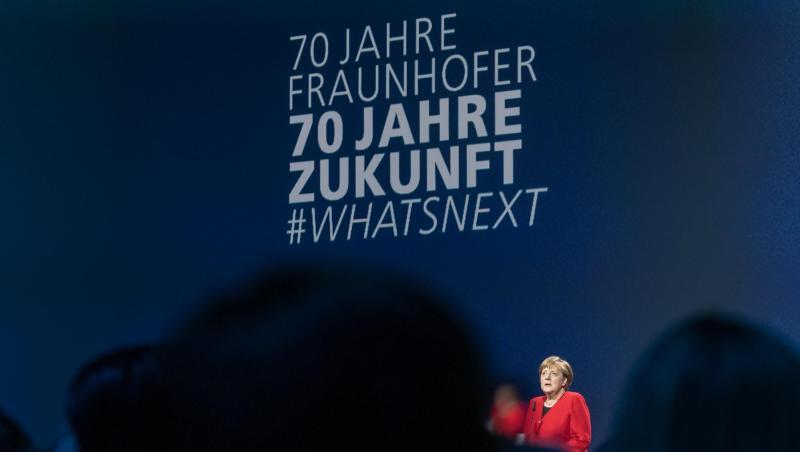 Angela Merkel (CDU) spricht während der Fraunhofer-Jahrestagung von einer Bühne aus, im Vordergrund Silhouetten von Zuhörern. Peter Kneffel Foto: Peter Kneffel
