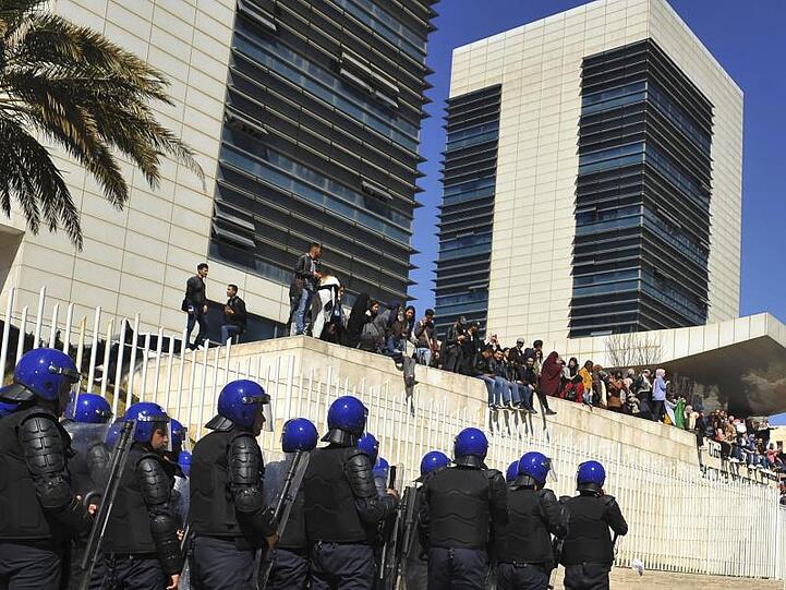 Polizisten sind in Algier aufgezogen und beobachten Demonstranten, die gegen eine erneute Kandidatur des algerischen Präsidenten Bouteflika protestieren.