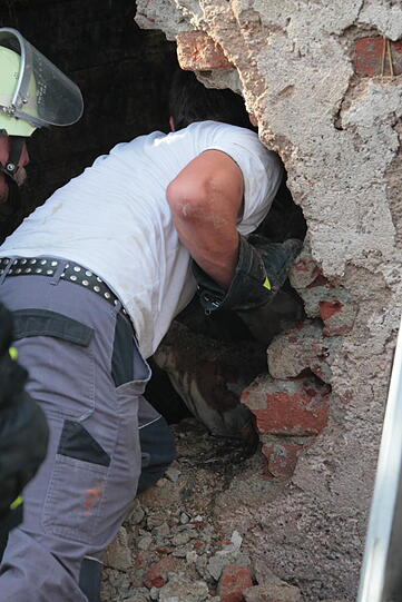Hinter einer eingestürzten Mauer im abgebrannten Bauernhof ist noch ein Kuhkalb eingesperrt. Mit bloßer Hand und einem Geißbein durchbrechen die Feuerwehrleute eine 50 Zentimeter dicke Mauer und retten es.
