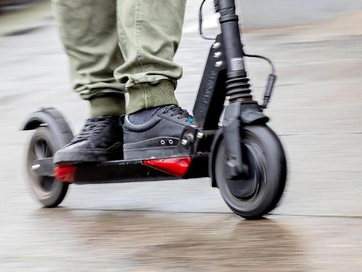 Ein Mann fährt mit einem E-Scooter auf dem Gehweg.