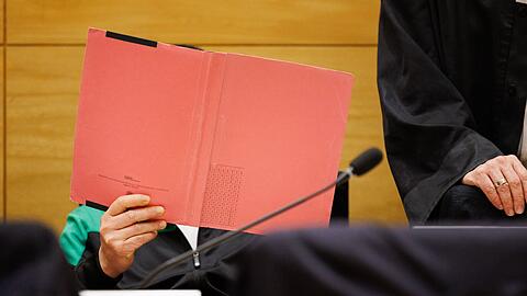 Einer der Angeklagten am Landgericht Bielefeld sitzt neben seinem Verteidiger und verdeckt sein Gesicht.