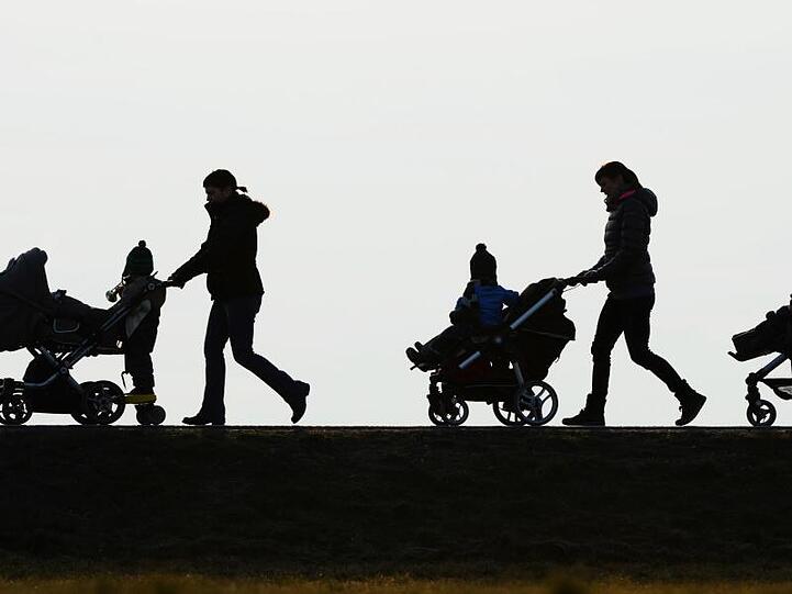 Drei Mütter schieben ihre Kinderwagen eine Landstraße entlang.