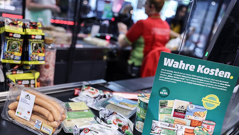 Produkte, deren Preis mit den verdeckte Kosten angepasst wurden, liegen auf einem Kassenband.