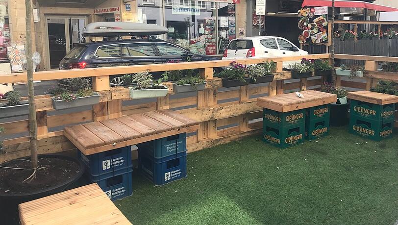 Bitte setzen: Leere Biertragl mit Holzplatten drauf, darunter Kunstrollrasen - hier können Anwohner sich jetzt zum Ratsch niederlassen.