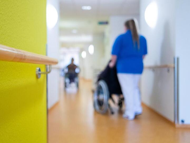 Eine Pflegerin schiebt eine Bewohnerin eines Pflegeheims in einem Rollstuhl über den Flur. Foto: Tom Weller/dpa/Archivbild