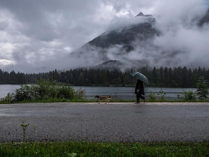 Eine Frau geht bei Regen mit ihrem Hund am Hintersee spazieren.
