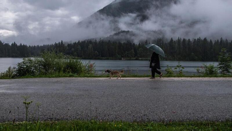 Eine Frau geht bei Regen mit ihrem Hund am Hintersee spazieren. Eine Frau geht bei Regen mit ihrem Hund am Hintersee spazieren.
