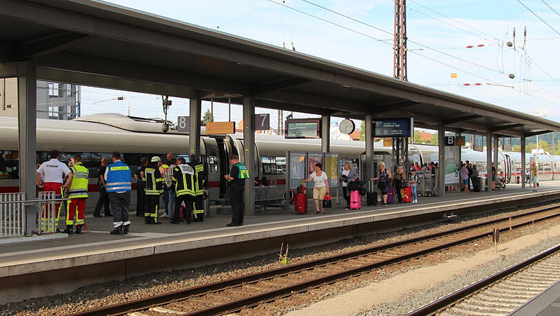 Einsatzkräfte der Feuerwehr und Zugpassagiere stehen am Sonntag auf einem Gleis des Hauptbahnhofs in Aschaffenburg.