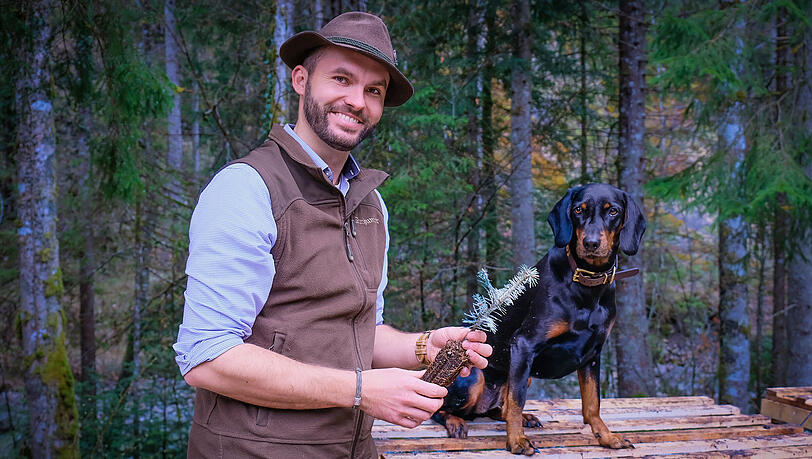F&ouml;rster Philip M&uuml;ller (32) leitet das Revier Jachenau der Bayerischen Staatsforsten. Neben ihm sitzt seine aufgeweckte H&uuml;ndin Xena. In der Hand h&auml;lt er eine kleine Tanne f&uuml;r die Fr&uuml;hjahrsbepflanzung. Bespr&uuml;ht ist sie mit Schafsfett und Sand zum Schutz vor Rehen.