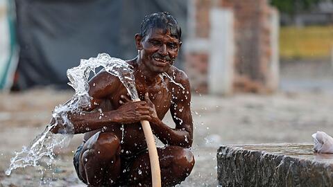 Ein Mann badet an einem öffentlichen Wasserhahn in der Nähe des Ganges in Prayagraj während eines heißen Sommertages.