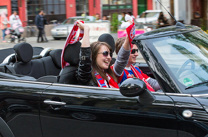 Zwei Fußballfans fahren am 26.04.2015 auf der Leopoldstraße in München (Bayern) und schwenken eine FC Bayern Schals. Bayern hat zum 25. Mal den Meistertitel gewonnen.