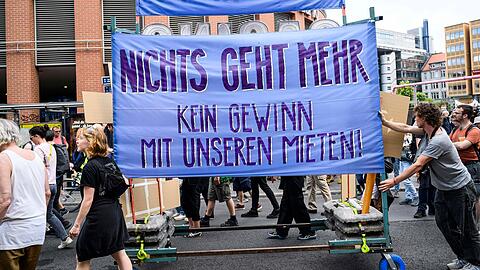 Menschen protestieren gegen hohe Mieten. Laut dem neuen Bericht verschärfen diese die Armut.