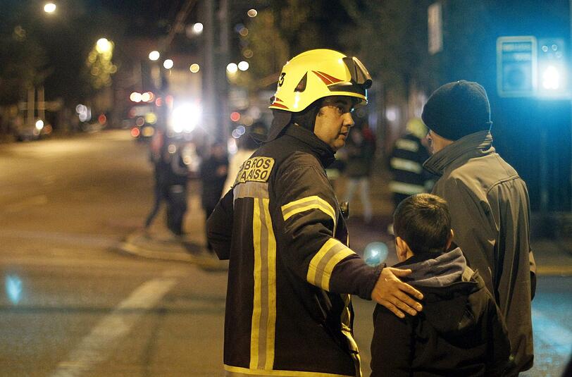 Ein Feuerwehrmann in Chile weist zwei Anwohnern den Weg aus der Gefahrenzone. Nach einem starken Beben vor der Nordküste Chiles wird großflächig evakuiert. Mindestens fünf Menschen sind ums Leben gekommen.