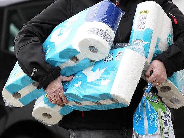 Ein Mann trägt Toilettenpapier und Küchenrollen aus einem Supermarkt.
