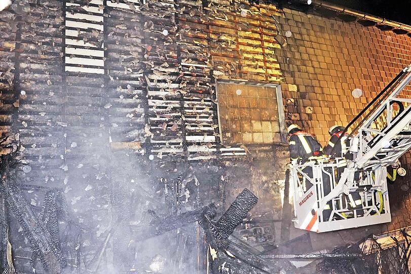 Feuerwehrleute bekämpfen von einer Drehleiter aus die letzten Flammen an einem Einfamilienhaus in Taufkirchen.