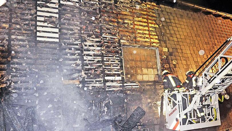 Feuerwehrleute bekämpfen von einer Drehleiter aus die letzten Flammen an einem Einfamilienhaus in Taufkirchen.