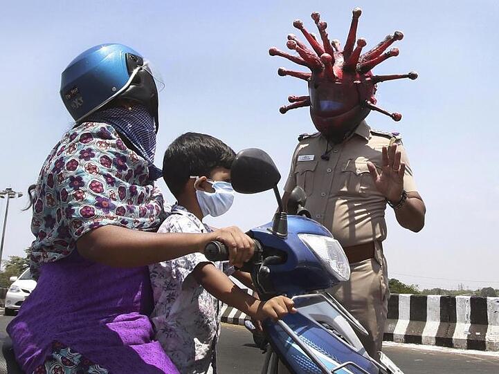 Ein Polizeibeamter im indischen Chennai trägt einen Helm, der einem Virus ähnelt, und weist Pendler auf die Einhaltung der Ausgangsbeschränkungen hin.