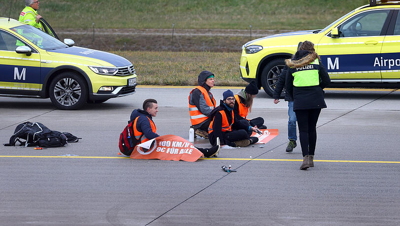 Vier Klimaaktivisten sitzen mit angeklebten Händen auf dem Zubringer einer Start-und Landebahn am Airport Franz-Josef-Strauß.