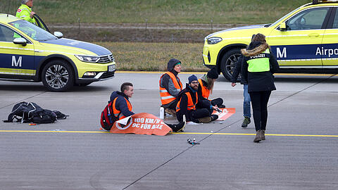 Vier Klimaaktivisten sitzen mit angeklebten Händen auf dem Zubringer einer Start-und Landebahn am Airport Franz-Josef-Strauß.