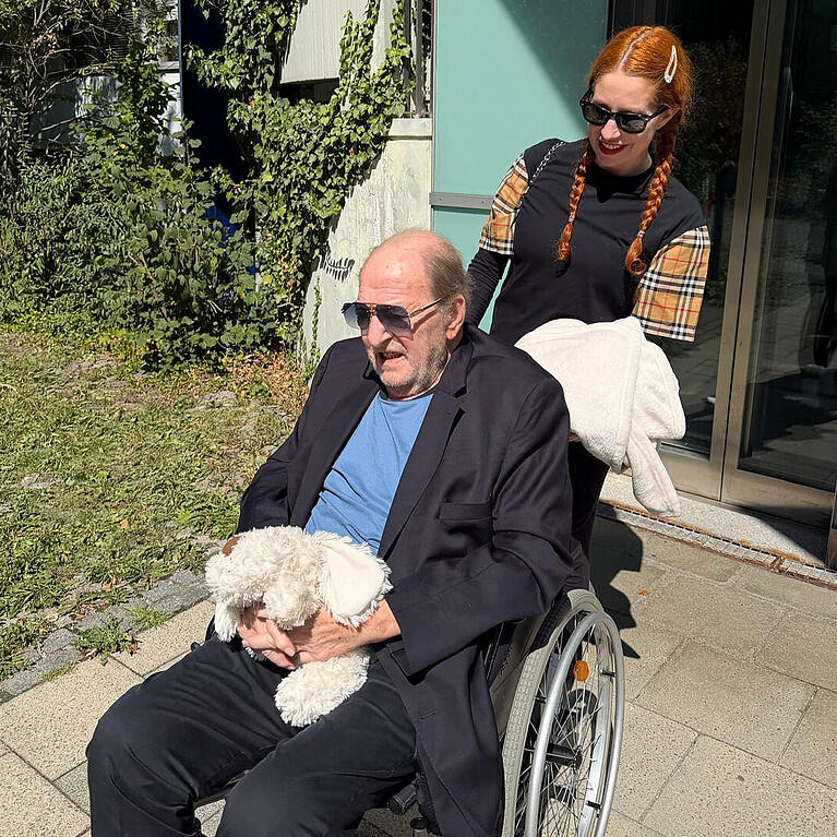 Ralph Siegel (80) wird von Ehefrau Laura (43) aus der Klinik abgeholt. Die ESC-Legende sitzt im Rollstuhl und h&auml;lt in den H&auml;nden Stofftier Hazy, welches an den verstorbenen Hund erinnert.