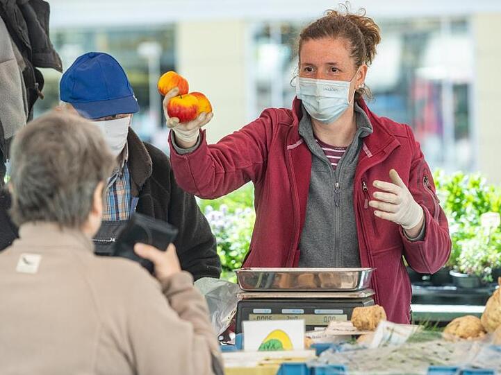 Die Verkäuferin eines Gemüsestandes in der Innenstadt spricht mit Schutzmaske zu einer Kundin. Foto: Armin Weigel/dpa/Archivbild
