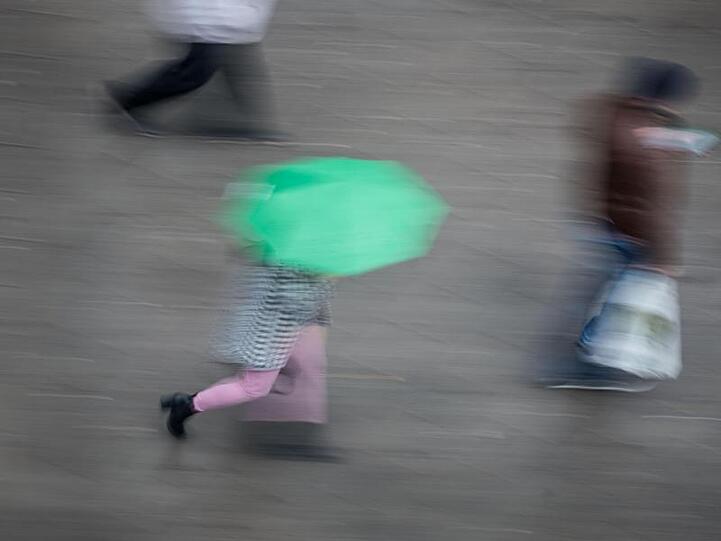 Eine Passantin geht mit ihrem Regenschirm eine Straße entlang.