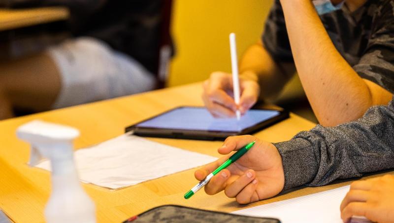 Ein Schüler hält beim Unterricht in seiner Klasse einen Stift, während ein anderer mit einem Tablet arbeitet.