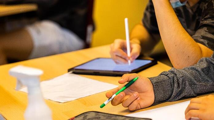 Ein Schüler hält beim Unterricht in seiner Klasse einen Stift, während ein anderer mit einem Tablet arbeitet.