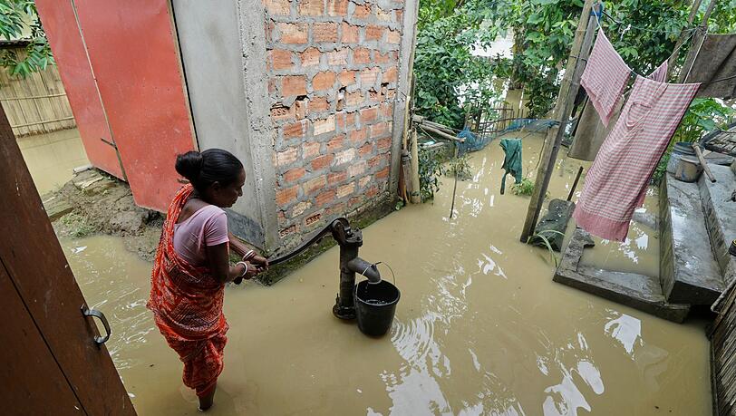 Eine Frau versucht in der überfluteten Umgebung ihres Hauses, Wasser zu sammeln.
