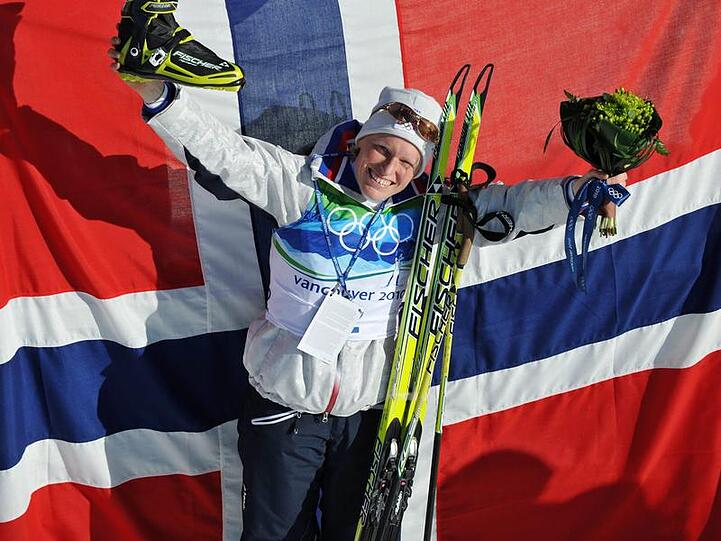 Olympiasiegerin Tora Berger posiert vor einer großen Norwegen-Fahne.