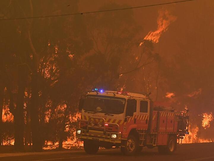 Ein Feuerwehrfahrzeug steht südwestlich von Sydney bei einem Buschbrand neben Bäumen, die Feuer gefangen haben.