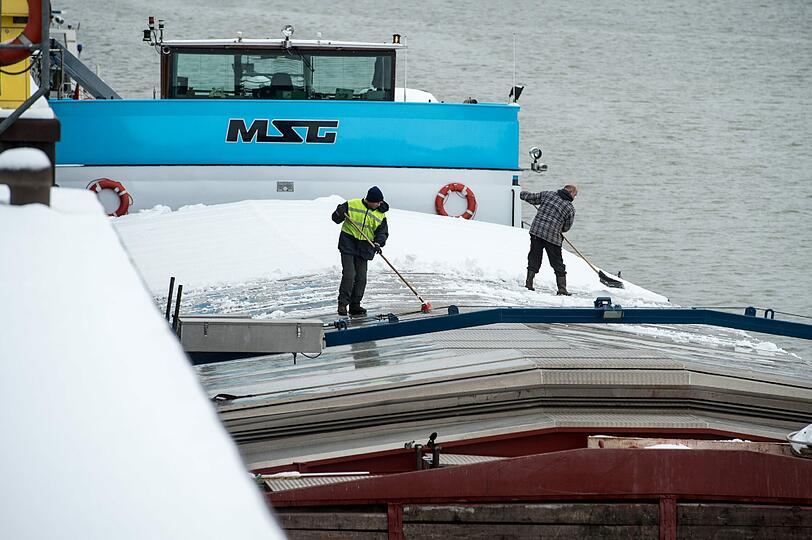 In Niederbayern sorgt der Schnee für Arbeit: Männer beseitigen  im Hafen in Straubing-Sand Schnee von einem Schiff.