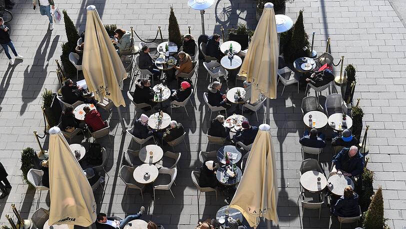 Gäste sitzen vor einem Café in der Sonne.