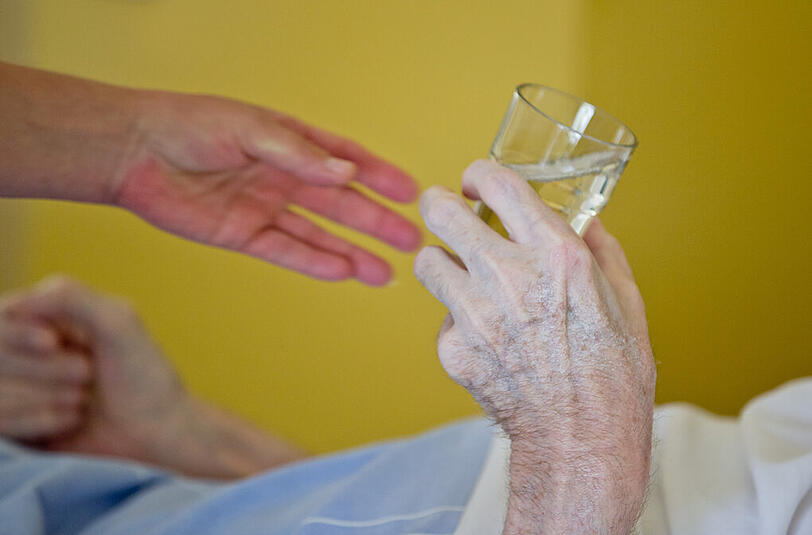 Eine Krankenpflegerin reicht einem Patienten auf einer Onkologie-Station ein Glas Wasser.
