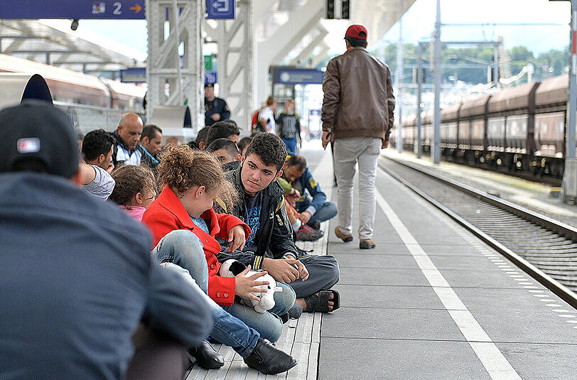 Flüchtlinge sitzen am Salburger Hauptbahnhof am Bahnsteig und warten. Deutschland hat am Mittwoch zum zweiten Mal seit Sonntag den Stop des Zugverkehrs aus Salzburg angeordnet.