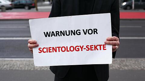 Ein Mann demonstriert am Rande einer Veranstaltung der Scientology-Sekte mit einem Schild gegen die Organisation.
