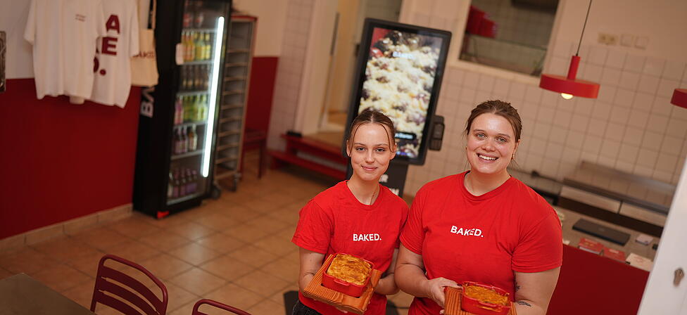 Hannah Eicher (r.) und Mitarbeiterin Lara pr&auml;sentieren die Aufl&auml;ufe bei Baked. In dem Lokal in der Maxvorstadt gibt es ausschlie&szlig;lich Gerichte aus dem Ofen.