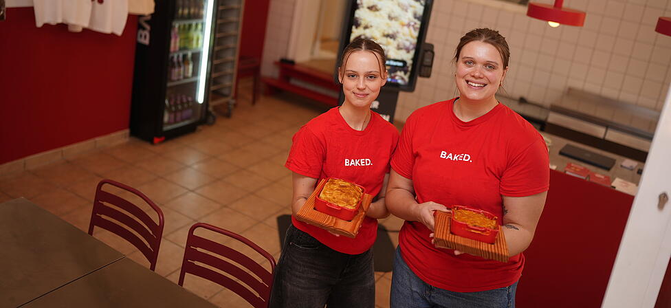 Hannah Eicher (r.) und Mitarbeiterin Lara pr&auml;sentieren die Aufl&auml;ufe bei Baked. In dem Lokal in der Maxvorstadt gibt es ausschlie&szlig;lich Gerichte aus dem Ofen.