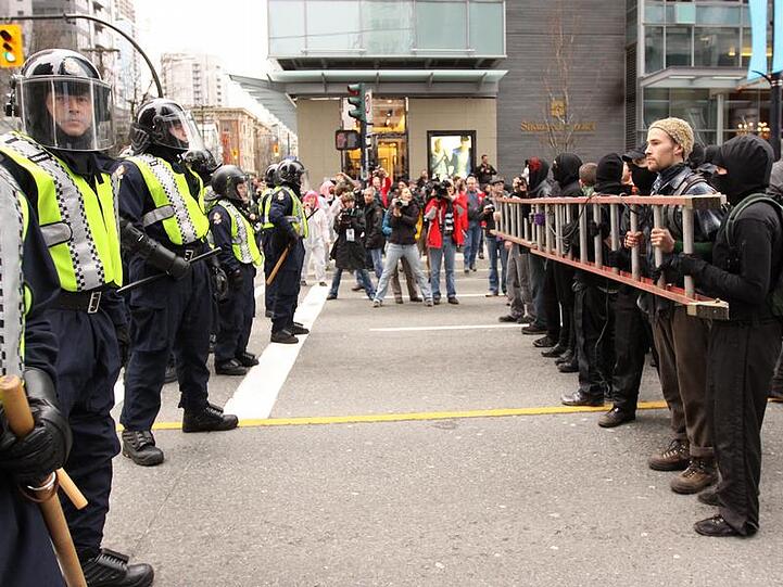 Die Polizei steht in Vancouver vermummten Demonstranten gegenüber.