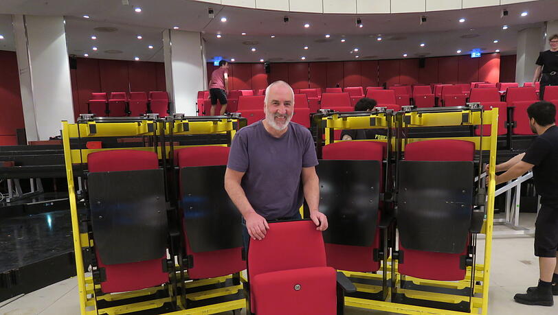 Leitet die aufwendige Rückverwandlung vom Ball- in den Theatersaal: Technik-Chef Hubert Schmid mit einem der unzähligen roten Theaterstühle, die wieder eingbaut werden müssen.