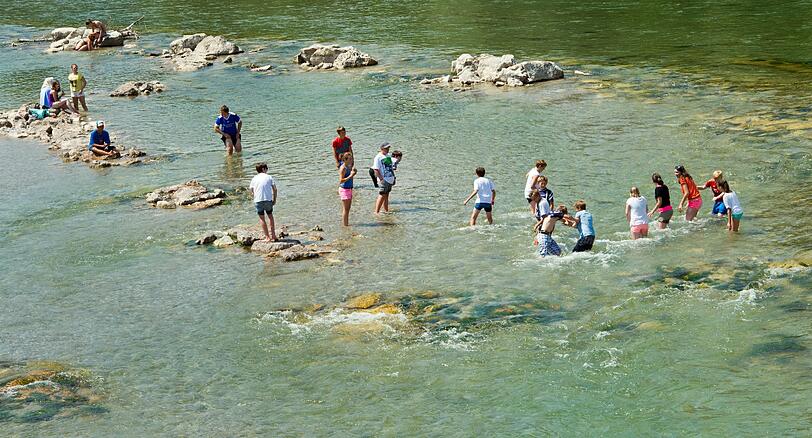 Eine Jugendgruppe watet durch das seichte grüne Wasser der Isar bei starker Strömung.