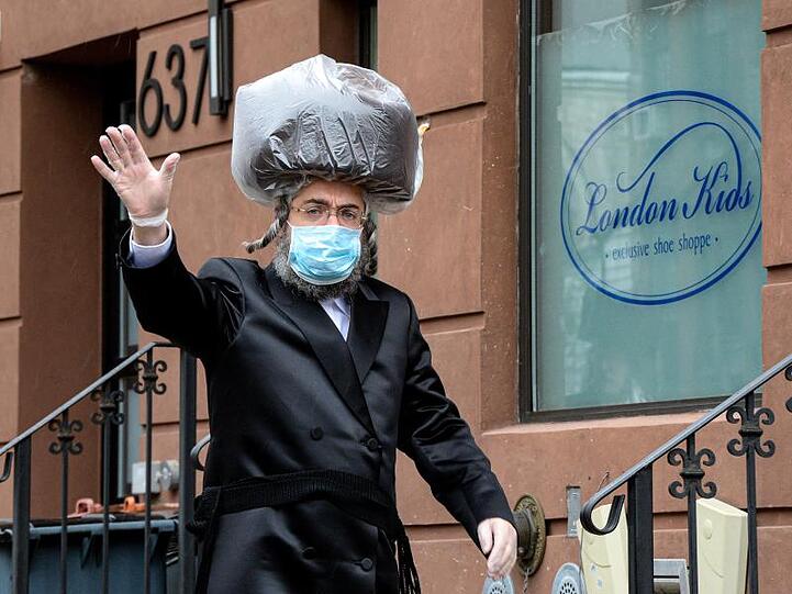 Ein chassidischer Jude in Brooklyn trägt einen Mundschutz, Handschuhe und einen Schutz über seinem Schtreimel, der traditionellen Kopfbedekung.