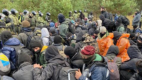 Migranten sitzen zusammen vor der Grenze in Belarus am gesperrten Übergang zu Polen.
