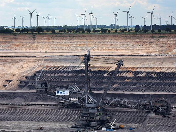 Braunkohlebagger im Tagebau Garzweiler, dahinter sind Windräder zu sehen.
