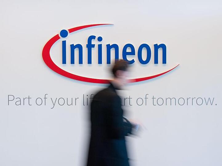 Besucher gehen während der Jahrespressekonferenz in der Zentrale vor dem Infineon-Logo entlang. Foto: Lino Mirgeler/Archiv