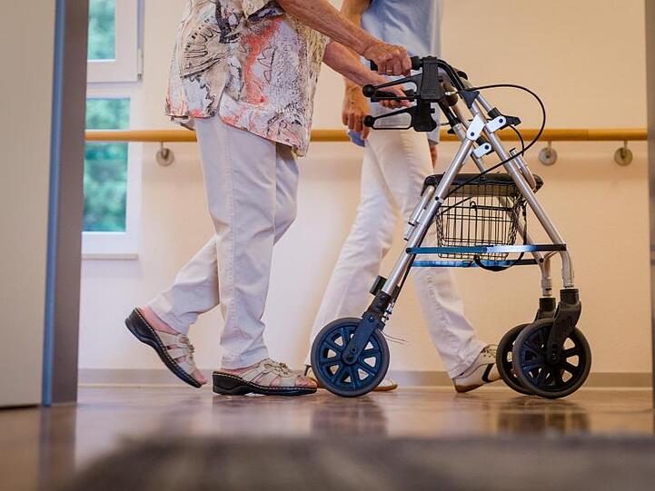 Eine Pflegekraft geht in einem Pflegeheim mit einer älteren Dame über einen Korridor. Foto: Christoph Schmidt/dpa/Symbolbild