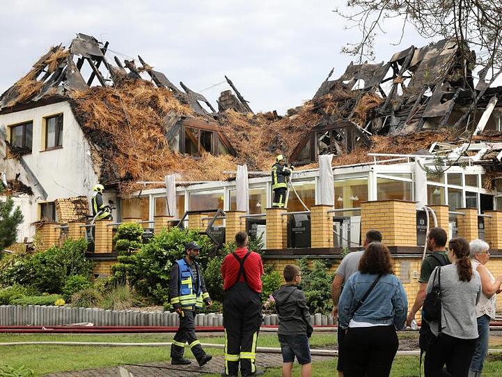 Urlauber und Feuerwehrleute stehen vor dem ausgebrannten Ostseehotel auf der Halbinsel Fischland-Darß-Zingst.