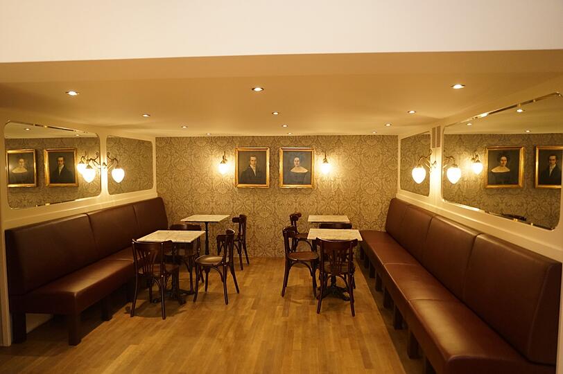 Traditionelle Kaffeehaus-Stühle im Stile Thonets und eine opulente Jugendstiltapete schaffen ein 20er-Jahre-Ambiente.